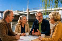 Zwei Frauen und Männer im Seniorenalter sitzen an einem Tisch mit der Jahrtausendbrücke im Hintergrund